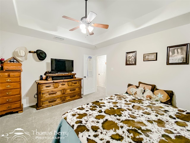 bedroom with ceiling fan, light colored carpet, and a tray ceiling