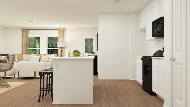 kitchen with white cabinetry, light hardwood / wood-style flooring, a breakfast bar area, and black appliances