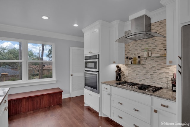 kitchen featuring wall chimney range hood, crown molding, stainless steel appliances, light stone counters, and white cabinets