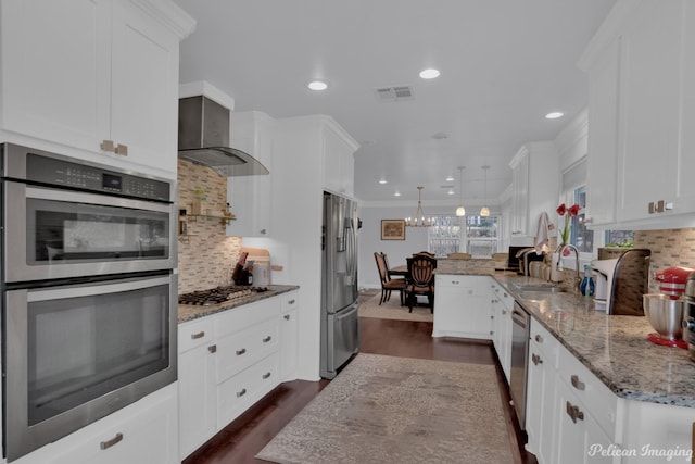 kitchen featuring pendant lighting, wall chimney range hood, sink, stainless steel appliances, and white cabinets