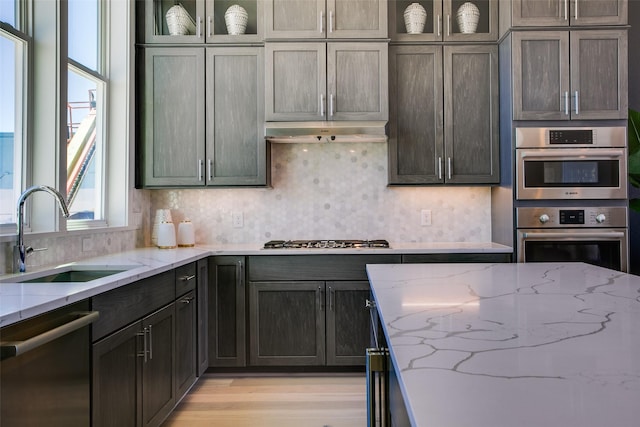 kitchen with sink, decorative backsplash, stainless steel appliances, and light stone countertops