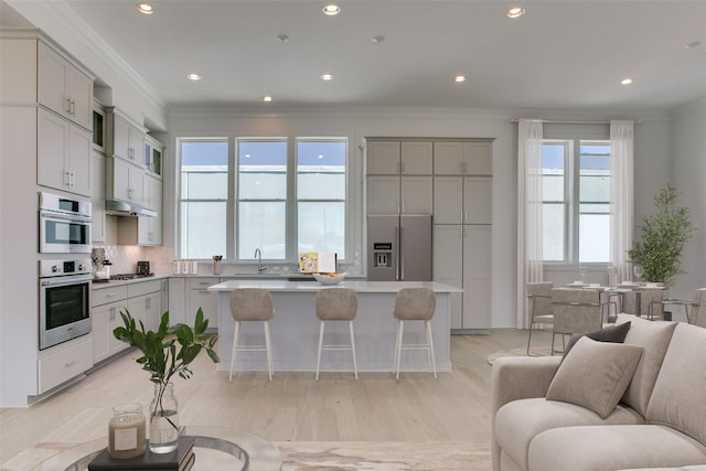 kitchen with crown molding, gray cabinets, a breakfast bar, stainless steel appliances, and a center island