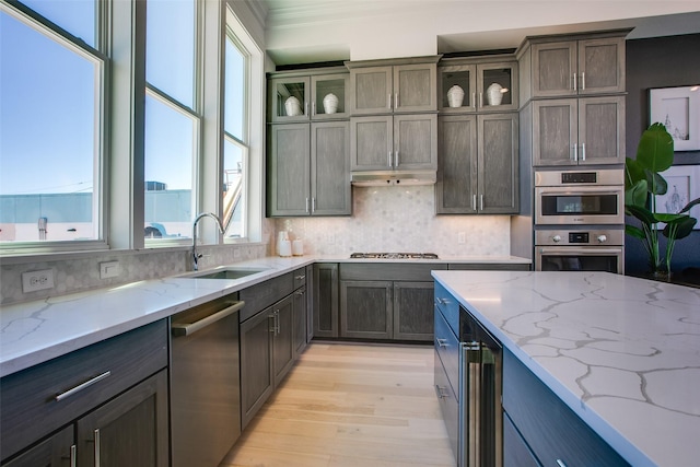 kitchen with light stone counters, dark brown cabinets, stainless steel appliances, light hardwood / wood-style floors, and decorative backsplash