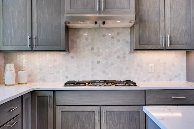 kitchen featuring stainless steel gas stovetop, light stone countertops, and backsplash