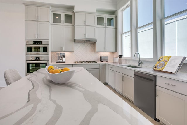 kitchen with sink, backsplash, stainless steel appliances, light stone counters, and white cabinets