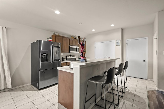 kitchen featuring stainless steel appliances, a kitchen bar, a kitchen island, and light tile patterned floors