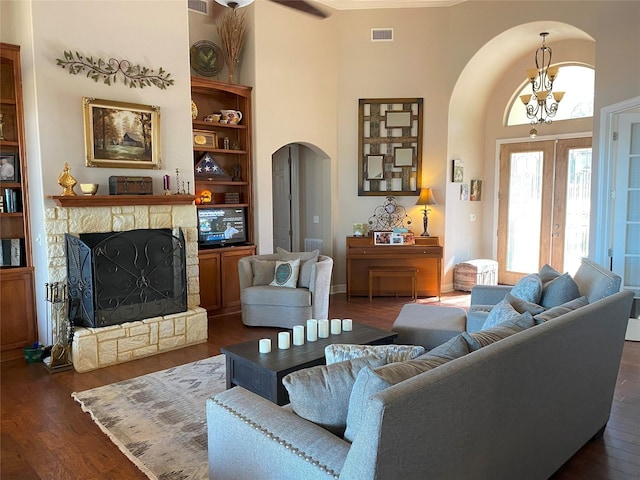 living room with an inviting chandelier, a high ceiling, built in shelves, dark hardwood / wood-style flooring, and a stone fireplace