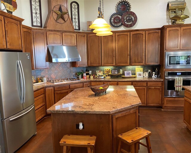 kitchen featuring light stone counters, decorative light fixtures, a center island, stainless steel appliances, and backsplash