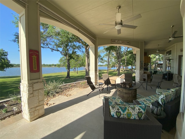 view of patio / terrace with a water view, ceiling fan, and an outdoor living space with a fire pit