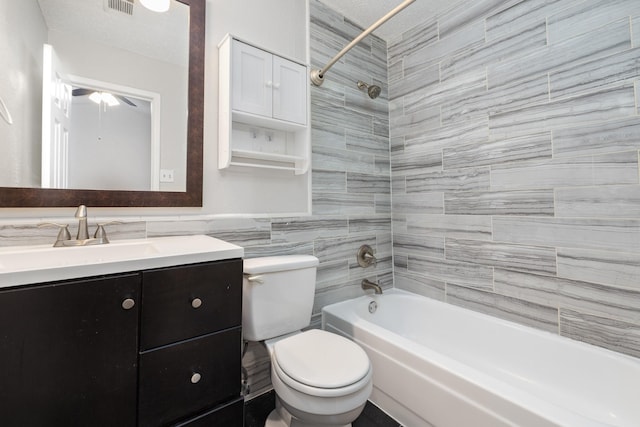 full bathroom featuring vanity, toilet, tiled shower / bath combo, and tile walls