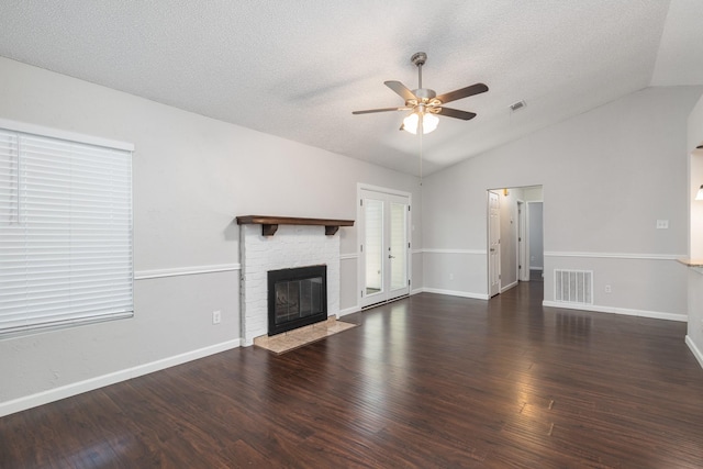 unfurnished living room with vaulted ceiling, ceiling fan, a brick fireplace, dark wood-type flooring, and a textured ceiling