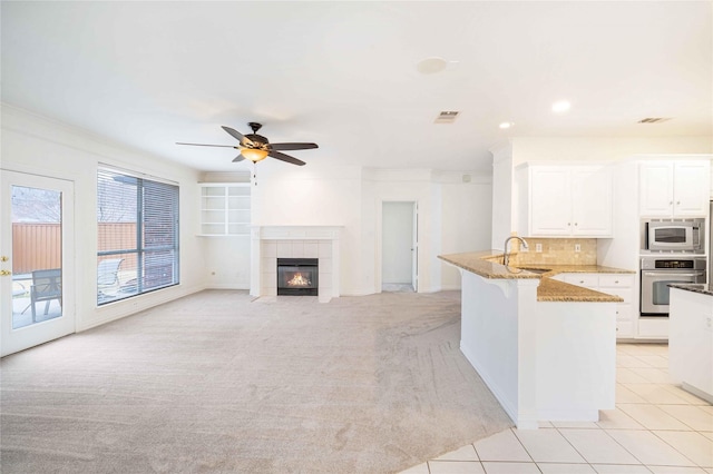 kitchen with white cabinetry, stainless steel appliances, light stone countertops, light carpet, and kitchen peninsula