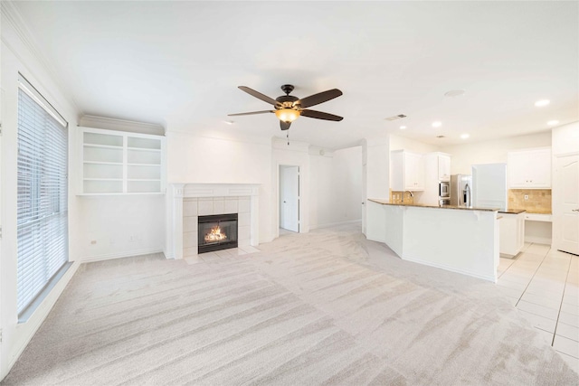 unfurnished living room featuring light colored carpet, a tile fireplace, and ceiling fan