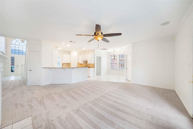 unfurnished living room with crown molding, ceiling fan with notable chandelier, and light colored carpet