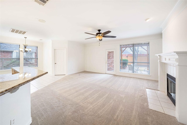 unfurnished living room with a tile fireplace, ceiling fan with notable chandelier, ornamental molding, and light colored carpet