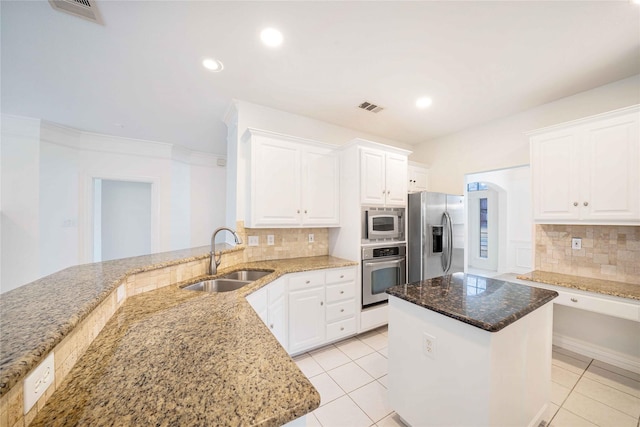 kitchen with appliances with stainless steel finishes, white cabinetry, sink, a center island, and light stone countertops