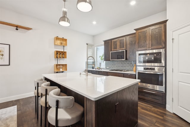 kitchen with dark wood-type flooring, stainless steel appliances, an island with sink, and dark brown cabinets