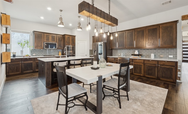 kitchen with a breakfast bar, dark brown cabinets, pendant lighting, stainless steel appliances, and a kitchen island with sink