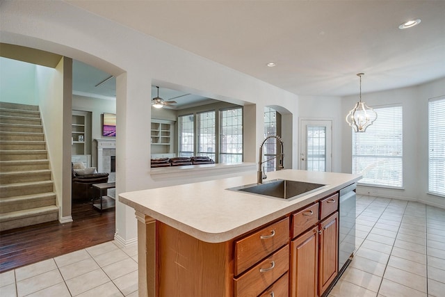 kitchen featuring light tile patterned flooring, sink, hanging light fixtures, a center island with sink, and stainless steel dishwasher