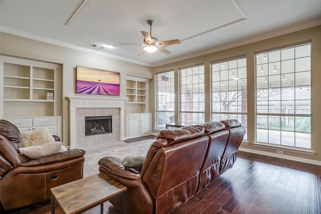 living room featuring hardwood / wood-style flooring, built in features, a tile fireplace, ceiling fan, and ornamental molding