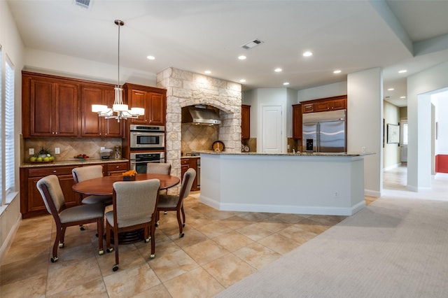 kitchen with an inviting chandelier, hanging light fixtures, stainless steel appliances, tasteful backsplash, and wall chimney exhaust hood