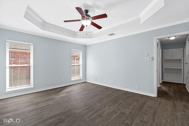 empty room with a raised ceiling, crown molding, dark wood-type flooring, and ceiling fan