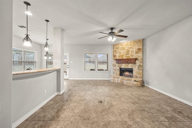 unfurnished living room featuring a stone fireplace, a textured ceiling, and ceiling fan