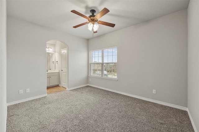 unfurnished bedroom featuring ensuite bath, light colored carpet, and ceiling fan