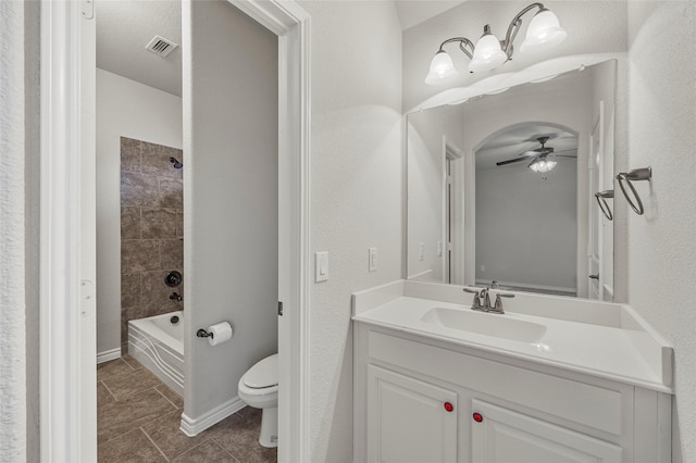 full bathroom with ceiling fan, tiled shower / bath, vanity, and toilet