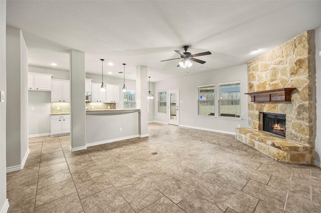 unfurnished living room featuring a stone fireplace, a textured ceiling, and ceiling fan