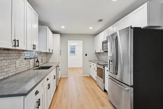 kitchen with appliances with stainless steel finishes, sink, dark stone countertops, white cabinets, and light hardwood / wood-style flooring