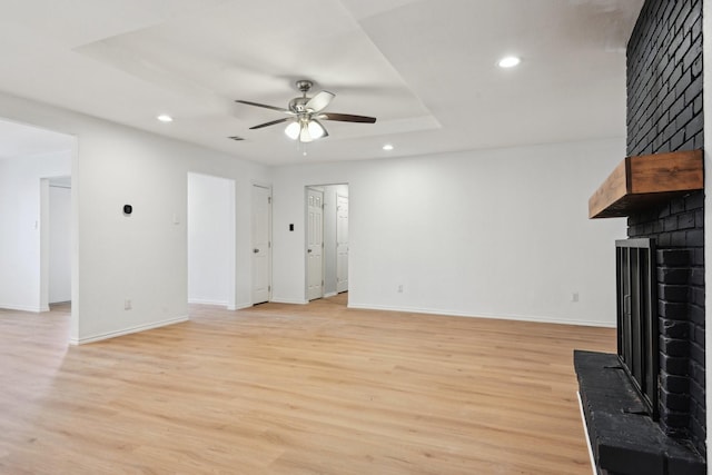 unfurnished living room featuring ceiling fan, a fireplace, a raised ceiling, and light wood-type flooring