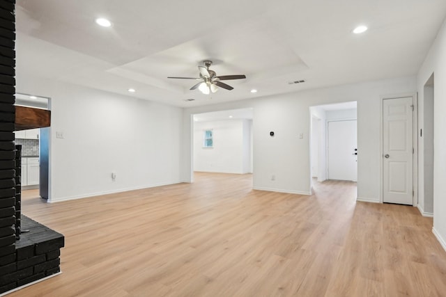 unfurnished living room featuring ceiling fan, a raised ceiling, and light wood-type flooring