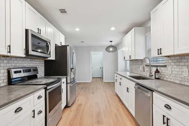 kitchen featuring white cabinetry, stainless steel appliances, decorative light fixtures, and sink