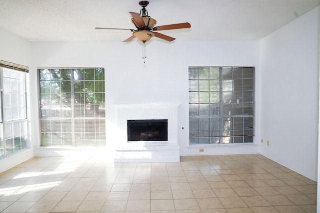 unfurnished living room featuring a brick fireplace, a wealth of natural light, ceiling fan, and light tile patterned floors