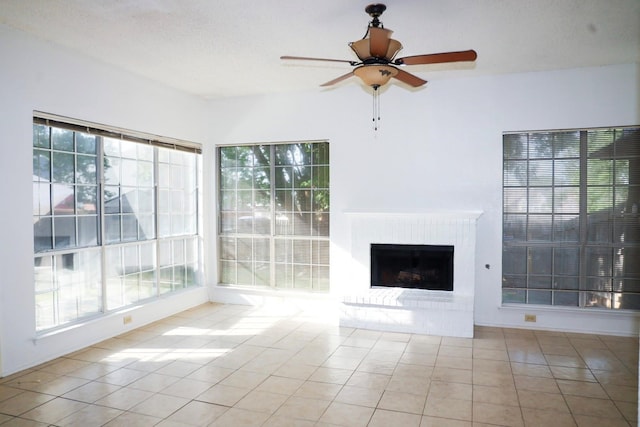 unfurnished living room featuring a brick fireplace, light tile patterned floors, a textured ceiling, and ceiling fan