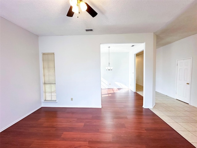 empty room featuring wood-type flooring, ceiling fan with notable chandelier, and a textured ceiling