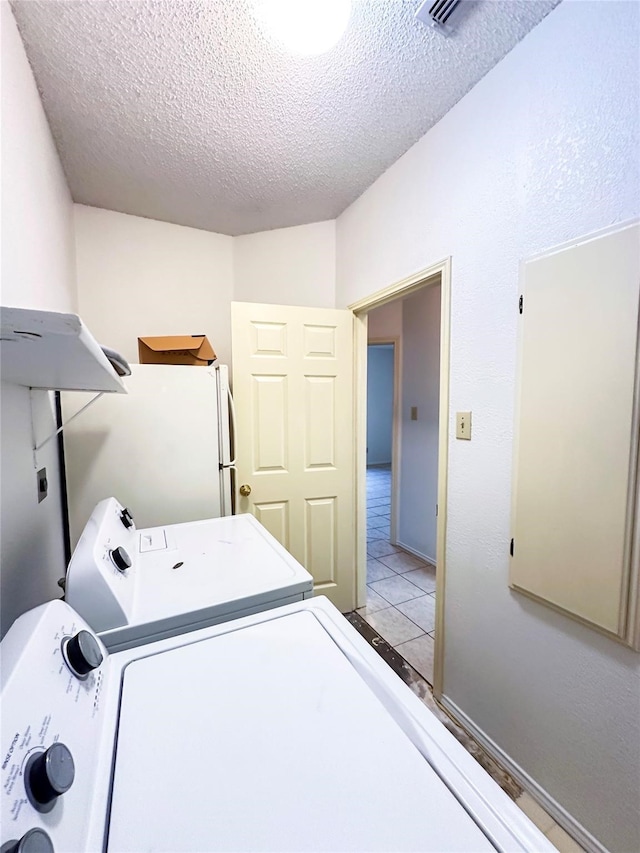 clothes washing area with washing machine and dryer, a textured ceiling, and light tile patterned flooring