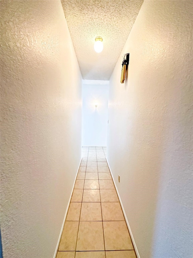 hallway with a textured ceiling and light tile patterned flooring