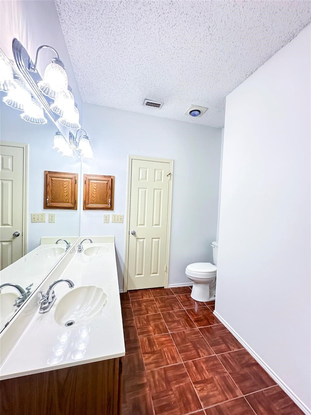 bathroom with parquet flooring, vanity, toilet, and a textured ceiling