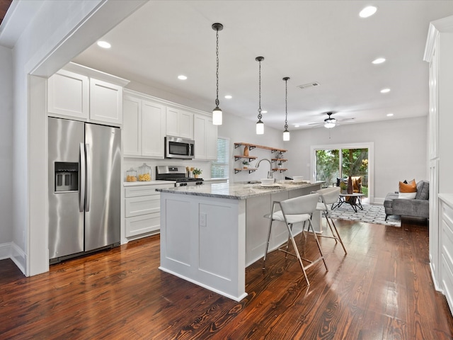 kitchen featuring hanging light fixtures, stainless steel appliances, light stone counters, an island with sink, and white cabinets