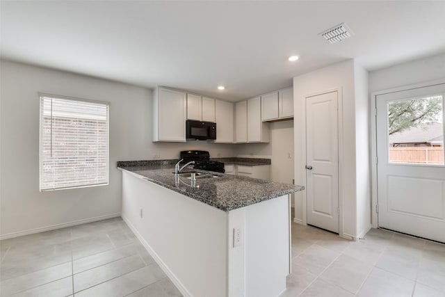 kitchen featuring dark stone countertops, sink, light tile patterned flooring, black appliances, and kitchen peninsula