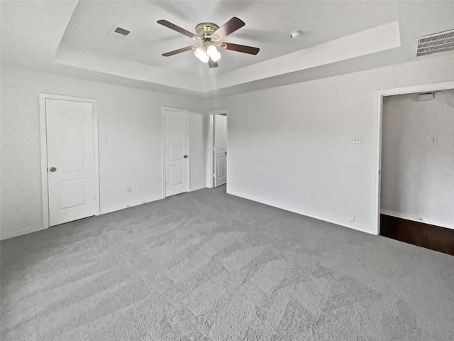 unfurnished room featuring a tray ceiling, ceiling fan, and carpet flooring