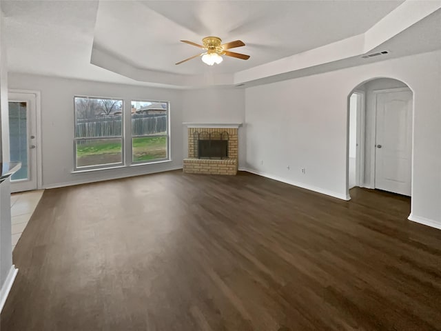 unfurnished living room featuring a raised ceiling, dark hardwood / wood-style flooring, ceiling fan, and a fireplace