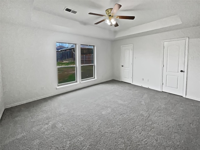 empty room with ceiling fan, a raised ceiling, and carpet floors