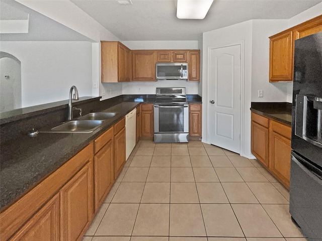 kitchen featuring stainless steel appliances, light tile patterned flooring, sink, and dark stone countertops