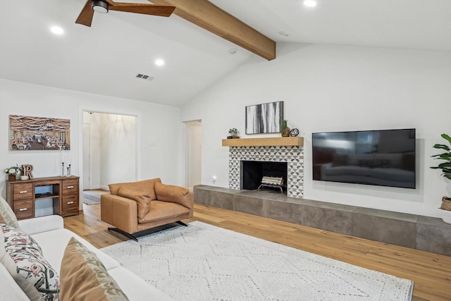 living room with vaulted ceiling with beams, ceiling fan, a tile fireplace, and light wood-type flooring