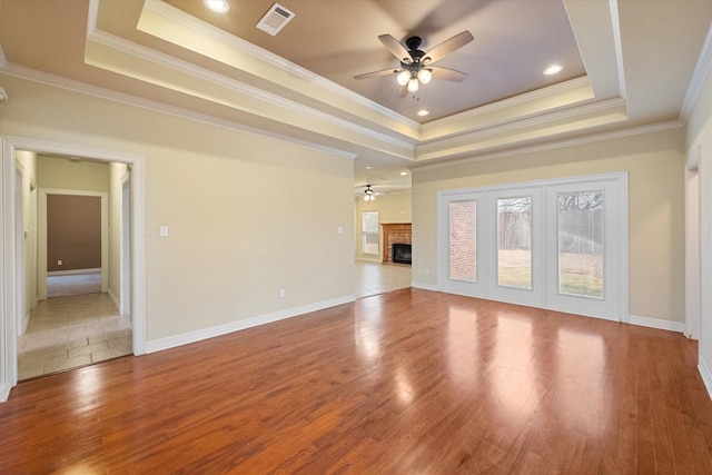 unfurnished living room featuring a tray ceiling, visible vents, wood finished floors, and a fireplace