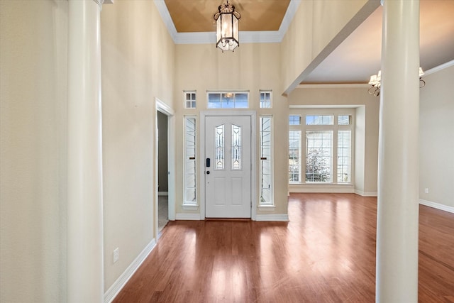 foyer featuring an inviting chandelier, ornamental molding, decorative columns, and wood-type flooring