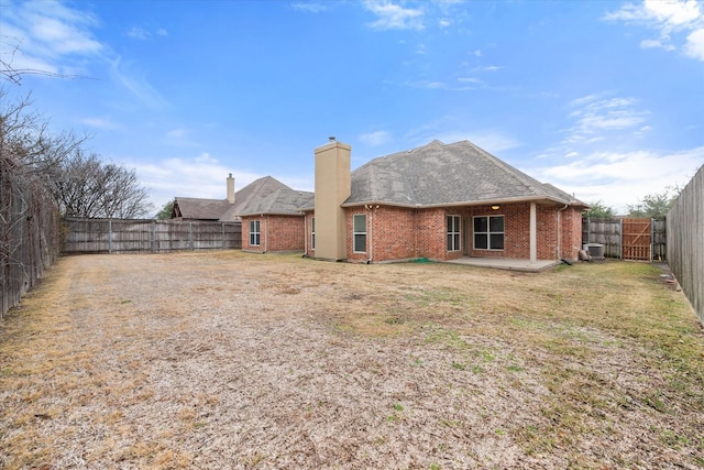 rear view of house with a fenced backyard, a yard, brick siding, a chimney, and a patio area